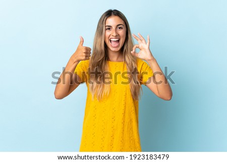 Young hispanic woman over isolated blue background showing ok sign and thumb up gesture