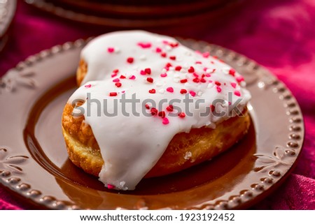 close up of heart donut with white icing running down topped with red, pink and white tiny heart sprinkles