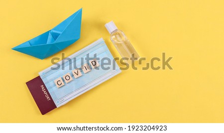 Passport with mask and paper boat with disinfectant on the left on a yellow background with space for text on the right, top view, close-up.