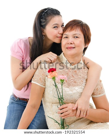 Senior mother holding carnation flower, adult daughter embraces and kissing mom, isolated on white background. Mixed race Asian family portrait. 