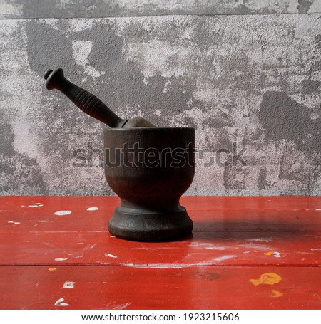 Manual metal grain grinder with bronze tones used in the kitchen for cooking, seasoning and aromas. On a red wooden table with small stains of handmade paint on a gray and white textured background.
