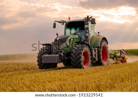 green tractor plowing cereal field with sky with clouds Royalty-Free Stock Photo #1923229541