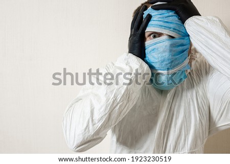 a frightened man in a protective suit hung with medical masks depicts horror against a white wall. The horrors of the epidemic, the danger of the coronavirus