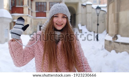 Woman tourist looking to camera, waving hi, hello, welcome, goodbye gesture sign while standing outdoors in winter. Caucasian pretty girl with smile on face posing on street in city. Positive emotions