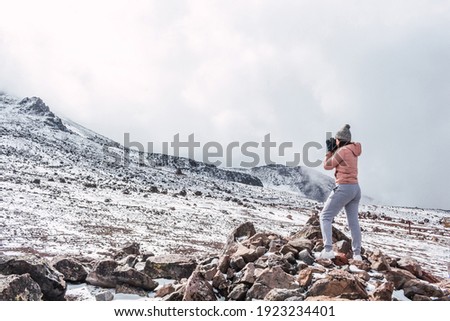 Woman photographer standing on some rocks taking landscape photos on a snowy mountain in the middle of the clouds