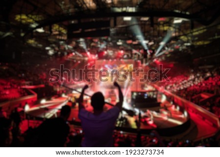 Abstract blurred background of big esports gaming event at big arena. Man with a hands raised. Royalty-Free Stock Photo #1923273734