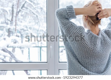 A woman looks out of the window at the snow-covered outdoors