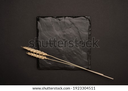 Mockup image. Square invitation card mock up with a golden ears branch. Top view of black stone plaque mockup with golden wheats on black table