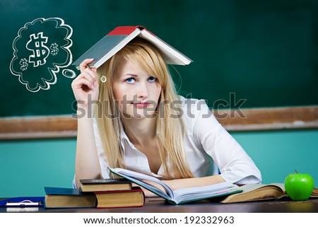 Closeup portrait business woman, student, teacher seating at desk thinking how to make money looking worried isolated green chalkboard background, bubble filled dollar signs. Facial expression emotion