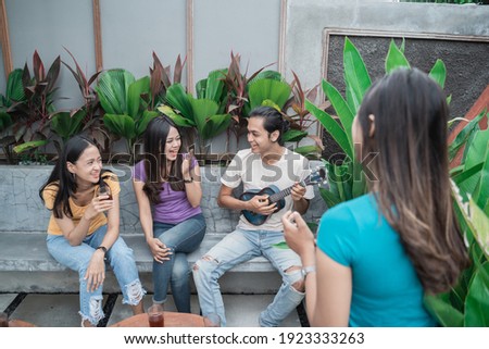 Group of asian friends having fun singing and playing guitar together in the backyard