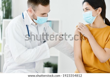 doctor's assistant injections in the shoulder of a woman wearing a medical mask covid vaccination