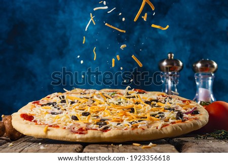 Pizza cooking sprinkled with cheese, frozen in motion on a blue background