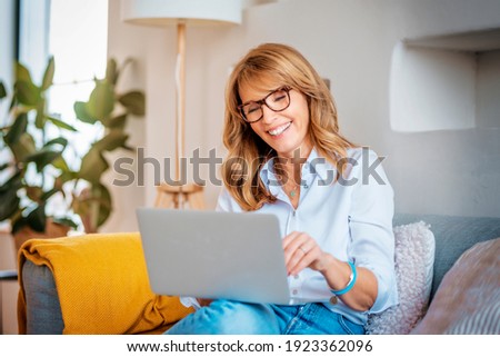 Shot of a happy middle aged woman using her laptop on the sofa at home.  Royalty-Free Stock Photo #1923362096