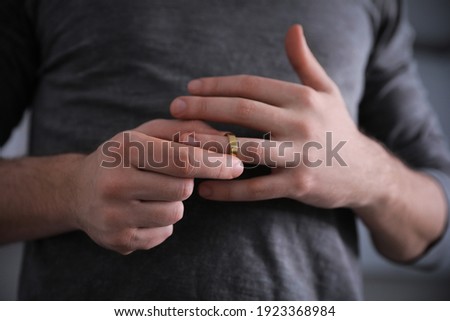 Man taking off wedding ring on blurred background, closeup. Divorce concept Royalty-Free Stock Photo #1923368984