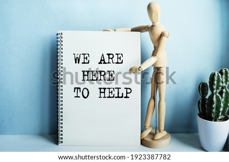 Wooden man next to a notebook, the inscription on the notebook has a financial or marketing concept. The inscription in the notebook WE ARE HERE TO HELP.