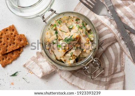 Pickled herring in a glass jar top view. Senapssill. Pickled herring with mustard, vinegar, onion, oil, dill, and sour cream. Scandinavian cuisine.  Royalty-Free Stock Photo #1923393239