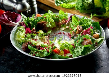 Warm salad mix with chicken liver and pomegranate served in a white plate on a dark marble background. Restaurant food.