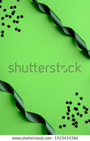 St Patrick's Day banner design. Frame made of green ribbon and shamrock shaped confetti on green background. Flat lay, top view, vertical. Minimal style.