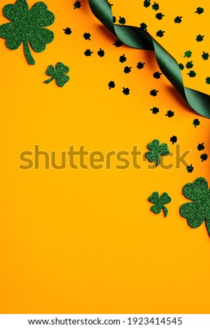 Saint Patricks Day orange background with shamrock leaves, green ribbon, confetti. Flat lay, top view, copy space. Happy St Patricks Day vertical banner design for social media stories. 