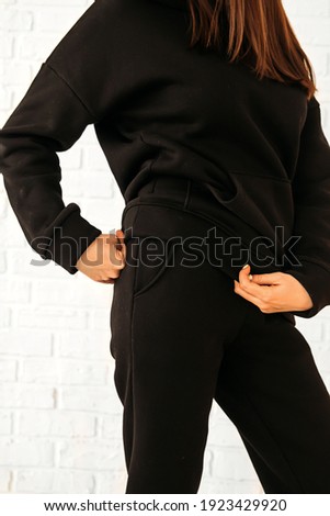 A girl in a black warm fleece tracksuit holds the bottom edge of the hoodie and shows the lines