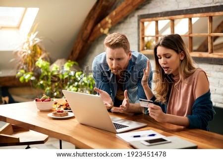 Displeased couple arguing while looking at their online bank account on laptop at home.  Royalty-Free Stock Photo #1923451478