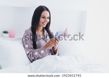Photo of pretty adorable young lady sleepwear sitting bed communicating modern device indoors room home