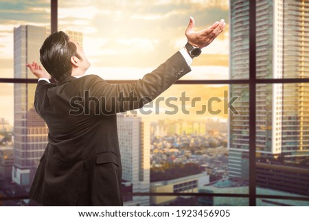Rear view of Asian businessman standing with raised hand on the office room