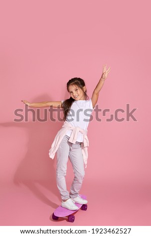 cute happy little child girl riding skateboard against pink background.