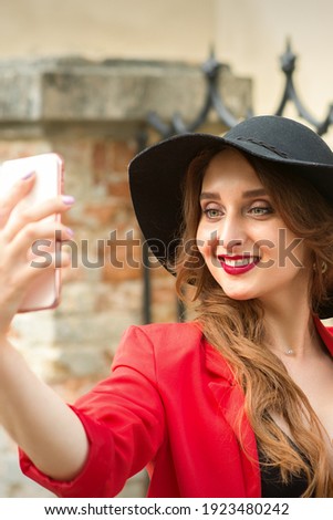 Beautiful smiling caucasian young woman taking selfie on the smartphone against an urban background