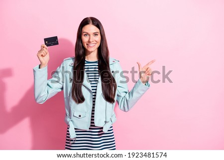 Photo of young happy woman wear striped dress blue leather jacket point empty space hold credit card isolated on pink color background