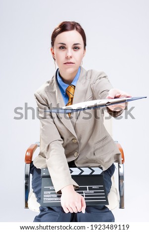 Filmmaking Concepts. Portrait of Young Caucasian Female Posing in Bright Beige Blazer in Chair with Actioncut Indoors. Vertical Image