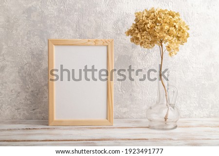 White wooden frame mockup with dried hydrangea in glass on gray concrete background. Blank, vertical orientation, still life, copy space.