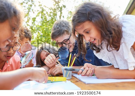 Inquisitive children look at leaf through magnifying glass and learn about plants and ecology Royalty-Free Stock Photo #1923500174