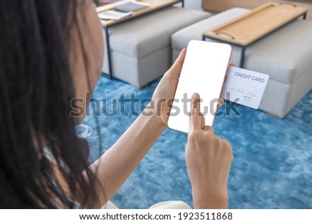 A woman shopping online on her sofa at home with a smartphone using a white credit card. And use your finger to tap the screen to verify the identity. Concept about business. Photo over shoulder shot.
