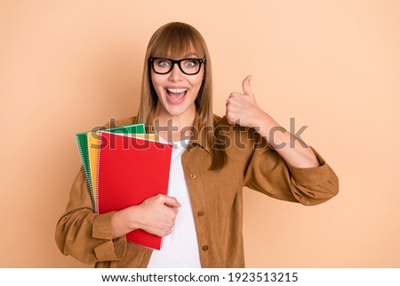 Photo of charming happy young woman make thumb-up hold notes isolated on pastel beige color background