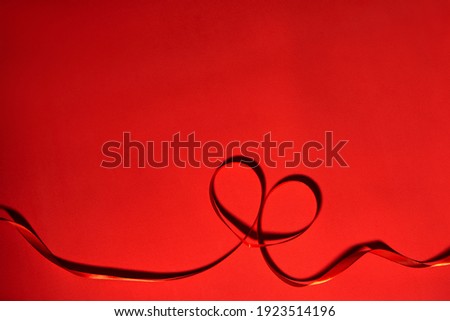 Heart made of red ribbon on red background, top view. Festive decoration. Heart shaped Ribbon. Valentines day greeting card
