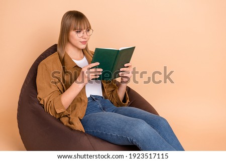 Photo of smart focused nice young woman hold book read wear glasses sit chair isolated on beige color background