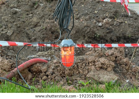 Red street lamp and police striped tape. A hole dug in the ground. Hazard warning concept.