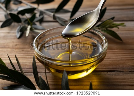 Spooning olive oil into a bowl placed on a wooden background Royalty-Free Stock Photo #1923529091