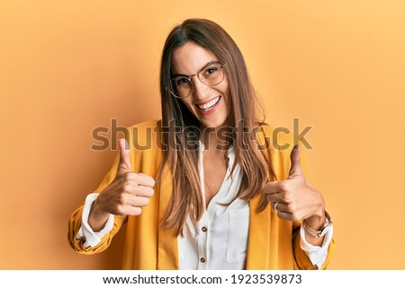 Young beautiful woman wearing business style and glasses success sign doing positive gesture with hand, thumbs up smiling and happy. cheerful expression and winner gesture. 