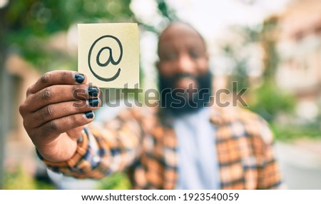 Handsome modern african american man with beard smiling positive standing at the street showing email symbol on paper