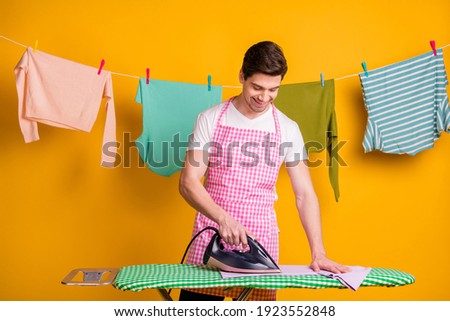 Photo of young happy handsome cheerful positive focused man ironing washed clothes isolated on yellow color background