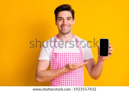 Photo portrait of guy demonstrating with hand showing phone with blank space isolated on vivid yellow colored background