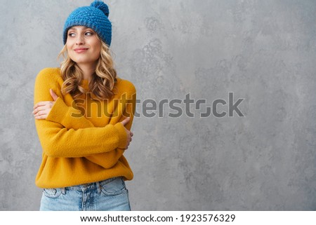 Happy beautiful woman smiling while posing in knit hat isolated over gray wall