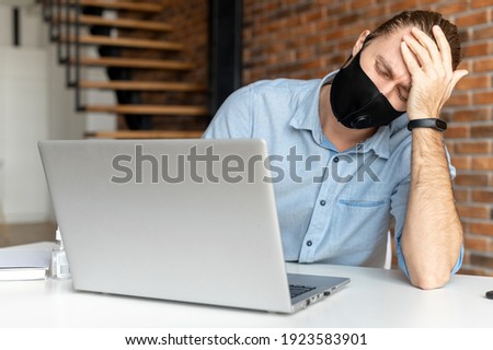 Disappointed businessman with hair pulled up, in mask, holding the head, looking at the computer screen, crisis in the company, working online, checking the balance on the bank account, use antiseptic