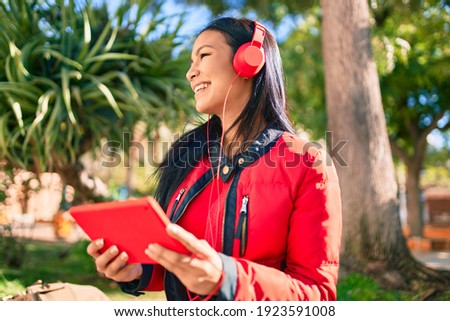 Young latin woman smiling happy using headphones and touchpad at the park.
