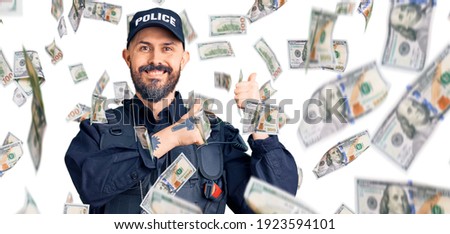 Young handsome man wearing police uniform pointing to the back behind with hand and thumbs up, smiling confident