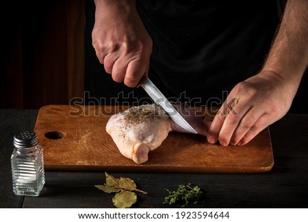 Cooking a chicken leg with the hands of a chef on a dark background. Cut the chicken meat with a knife. Free advertising space for a restaurant