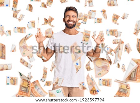 Young hispanic man wearing casual white tshirt gesturing finger crossed smiling with hope and eyes closed. luck and superstitious concept.