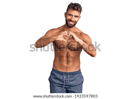 Young hispanic man wearing swimwear shirtless smiling in love doing heart symbol shape with hands. romantic concept. 